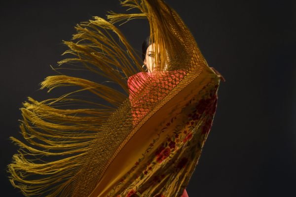 Flamenco dancer performing with a dramatic fringed shawl, capturing passion and movement in dynamic performance Flamenco dancer moving gracefully, her vibrantly patterned fringed shawl swirling dynamically against a dark background, embodying Spanish culture and passion